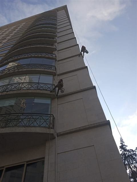 Técnicos de JONAMI pintando la fachada de un edificio alto suspendidos con cuerdas