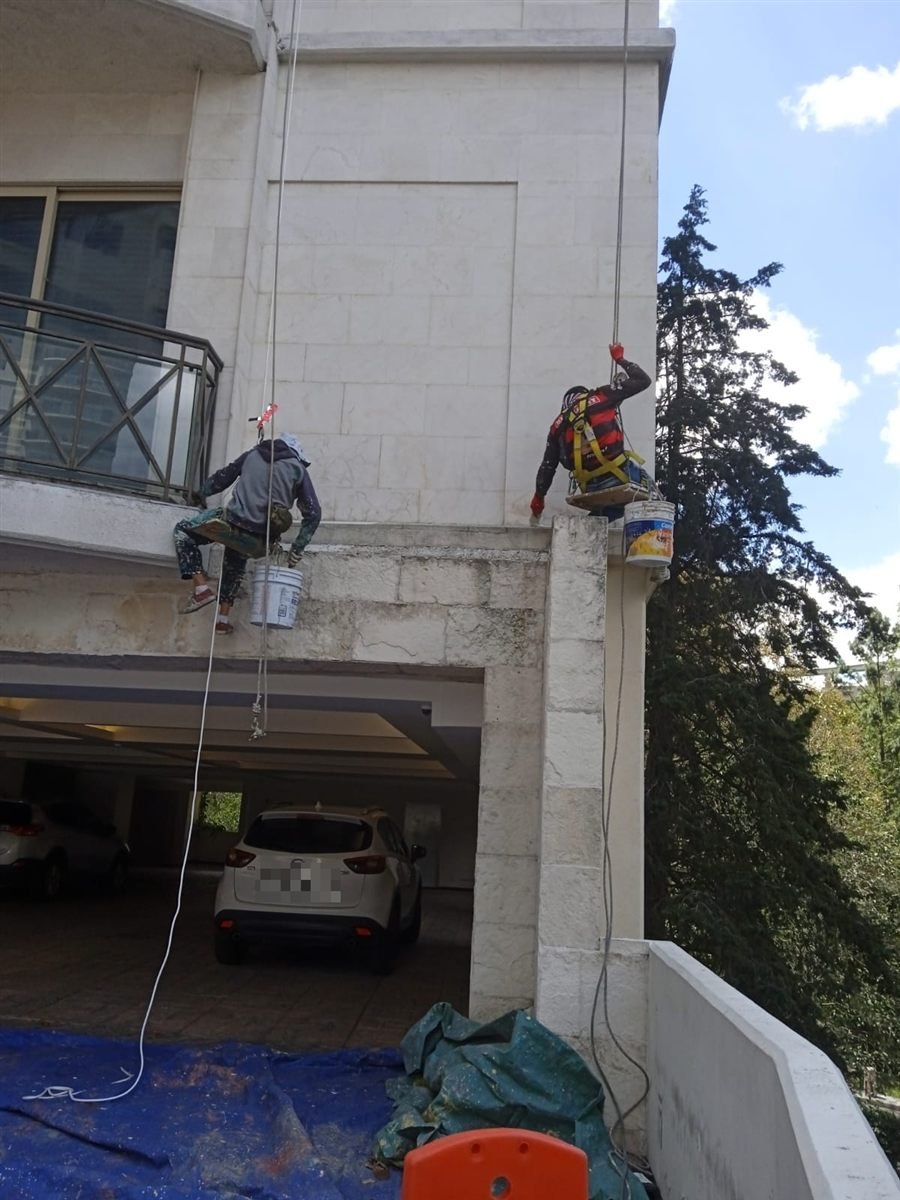 Técnicos de JONAMI con arnés trabajando en la fachada de un edificio residencial